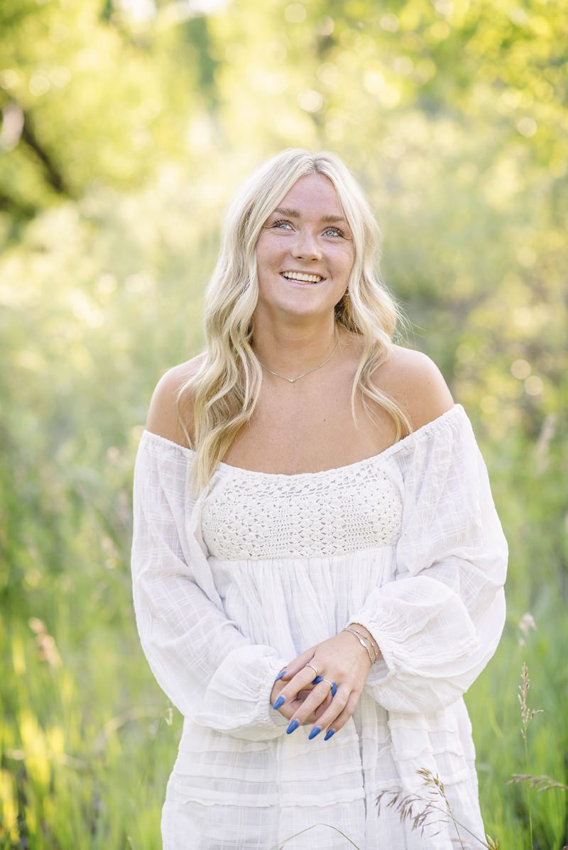 blond hair senior girl wearing white off teh shoulder dress in nature, smiling